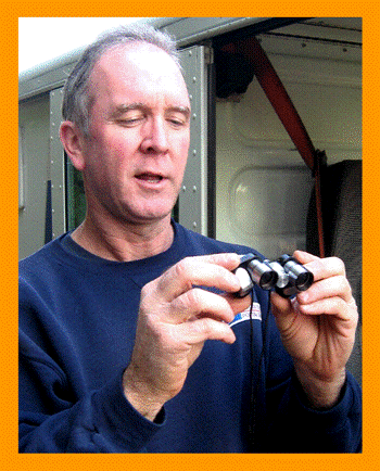 Mailman Examining Miniature Binoculars.
Mann mit  fernglas.
Homme avec jumelles.
Hombre con binoculares.
Hombre con prismaticos.
Man med kikare.
L'uoma col il binocolo. 